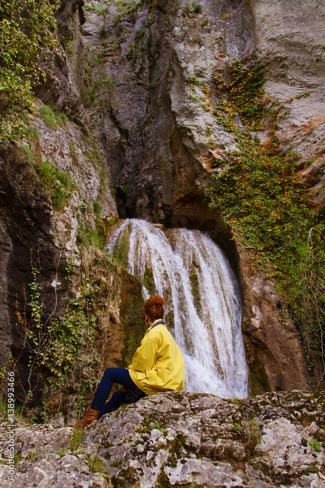 Naklejka premium Chica joven de espaldas a la cámara mirando una cascada en una montaña