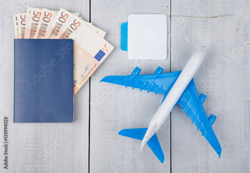 plane, passport, sketchbook and paper money on white wooden table