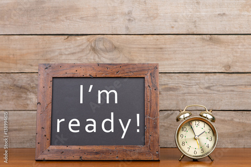 Alarm clock and blackboard with text "I'm ready" on brown wooden background