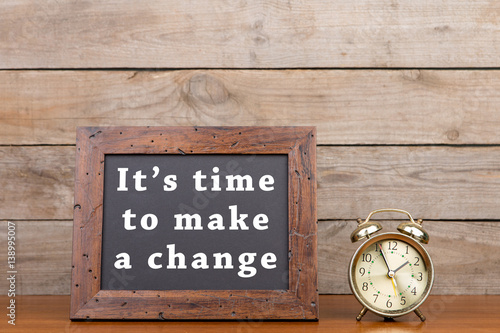 Alarm clock and blackboard with text "It's time to make a change"