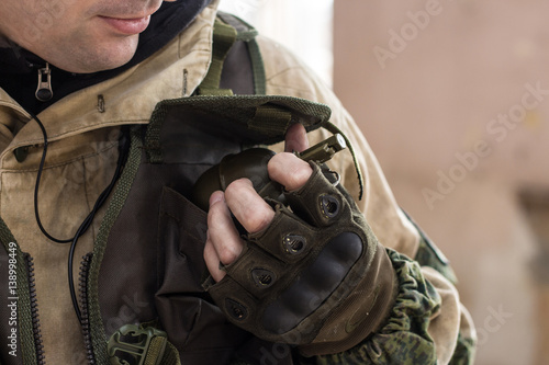 Crop shot of warrior holding sport grenade in his arm. Paintball.