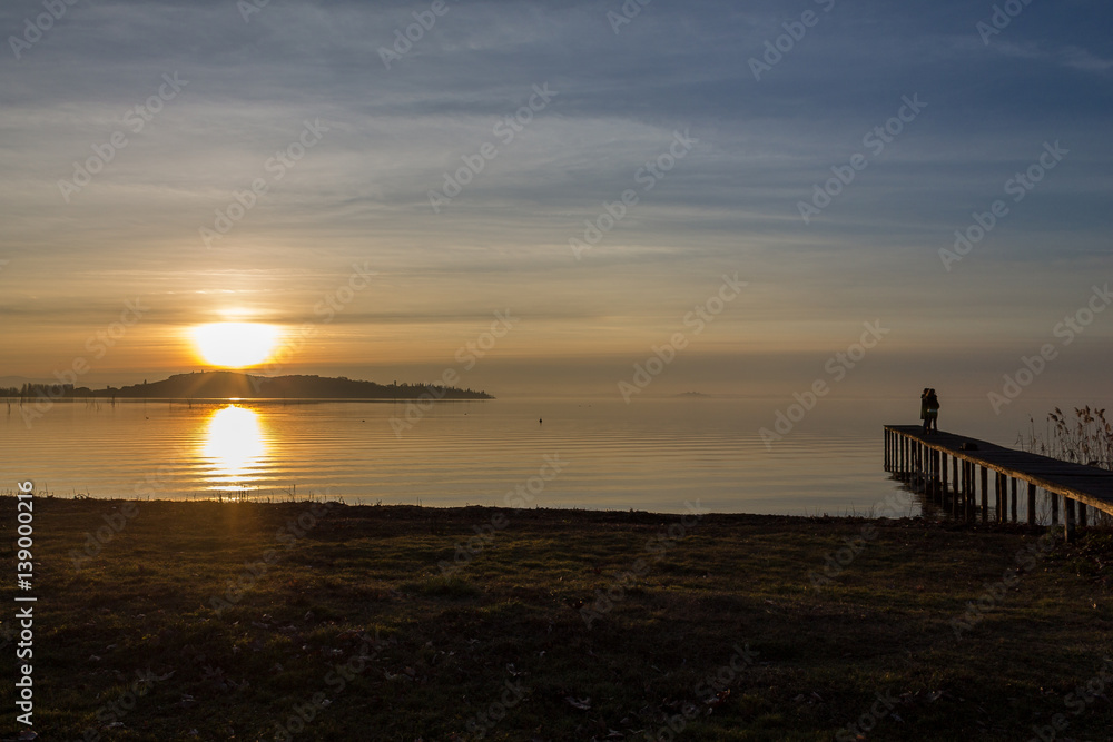 A couple on a pier on the lake during the sunset