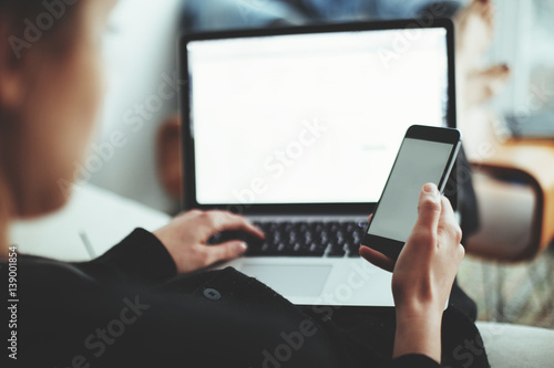 A woman sitting with mobile phone and laptop. Manager doing job at loft office. Soft focus