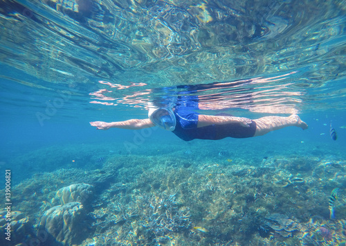 Woman swims undersea in swimming costume and full-face mask.