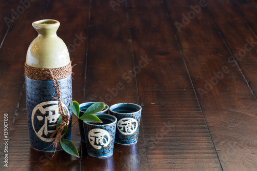 A bottle of sake and three sake cups on the rustic wood table.