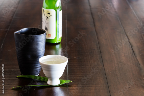 Black and white Japanese sake set and a bottle of sake on the rustic wood table.