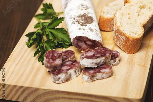 Fuet with bread on a wooden board. Spanish sausage.