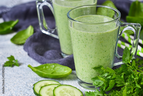 Green vegetable smoothie with avocado, cucumber and spinach on a gray background