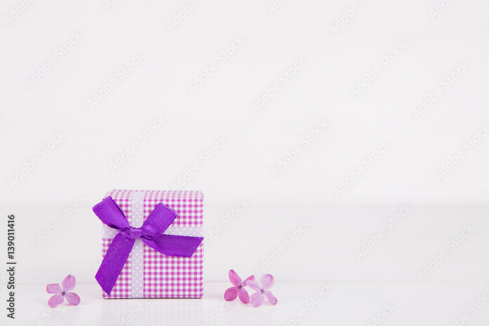 Purple gift box surrounded by lilac flowers on white background