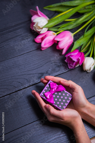 Gift box in hands with bouquet of pink tulips on dark wooden background