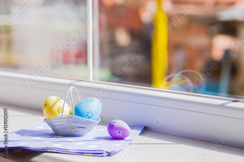Colorful easter eggs in white basket on blue fabric near window