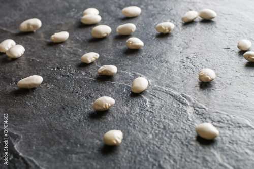 White beans are scattered randomly on a black stone table from slate.