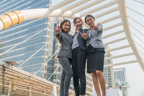 Three asian business women doing hand as a symbol standing smiling in modern city.