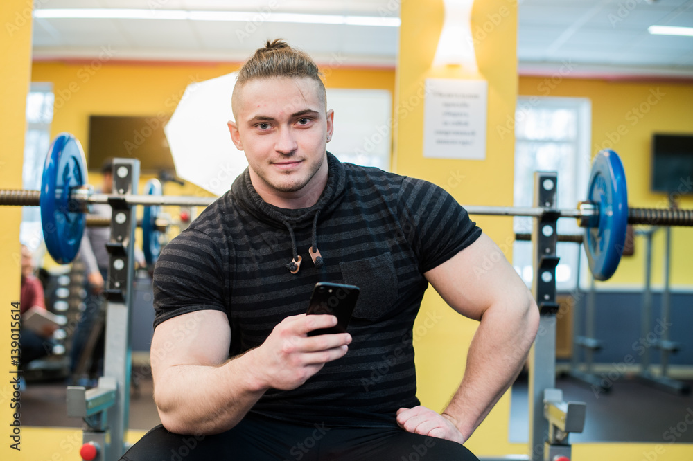 Young handsome man using phone while having exercise break in gym. Young handsome man using phone while having exercise break in gym.