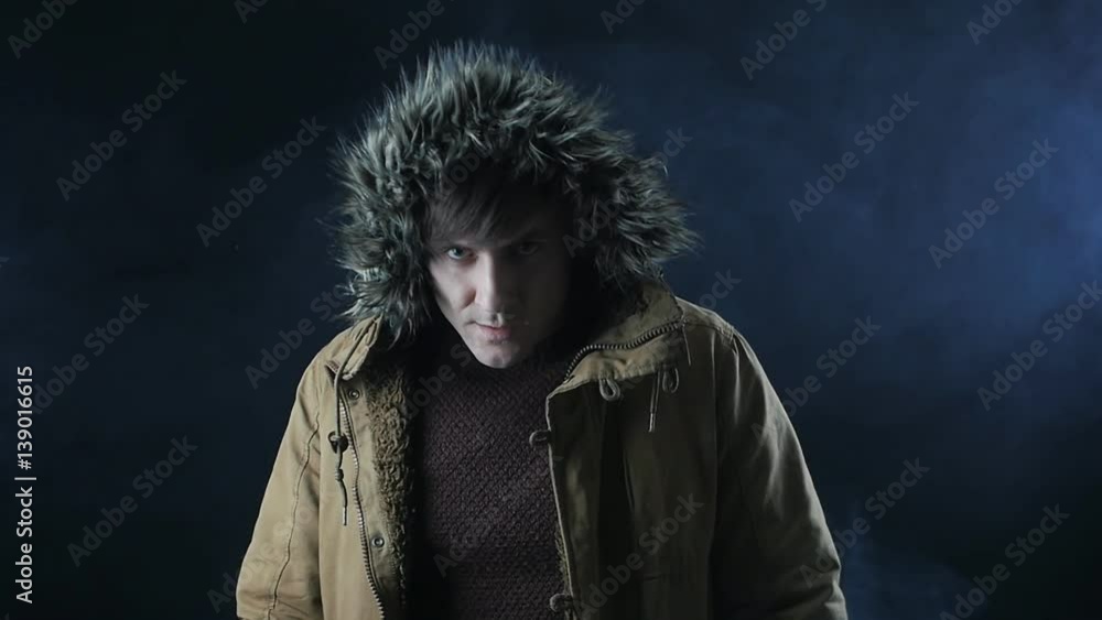 young man in a hood looks up in a dark mysterious room filled with smoke young man in a hood looks up in a dark mysterious room filled with smoke