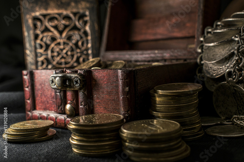 Treasure chest, pile and pillar of coins, a ceramic bowl filled with jewelry coins and candle lamp in dark environment 