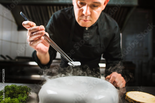 Chef is concentrated on preparing modern molecular dish with pincers and liquid nitrogen