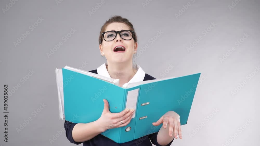 Woman office worker agent holding blue file folder in hands. Young tired overworked businesswoman or secretary with documents bills. Funny confused face expression. Business and paperwork on grey Woman office worker agent holding blue file folder in hands. Young tired overworked businesswoman or secretary with documents bills. Funny confused face expression. Business and paperwork on grey