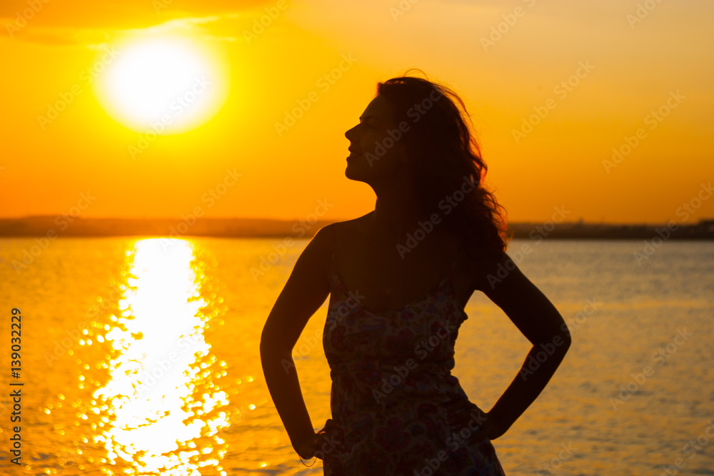 beautiful woman watching the sunset while sitting near the water