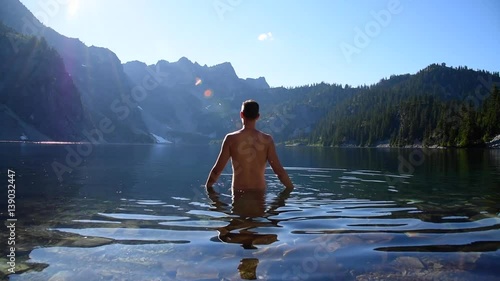 Real view of tall athletic man standing in a pristine alpine lake and raising arms
