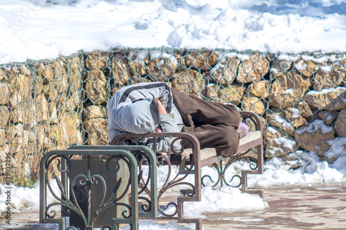 homeless sleeps on a bench in the park in winter photo