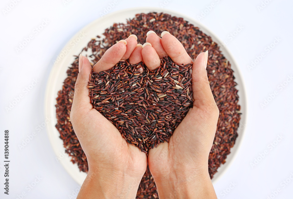 Fototapeta premium Hand holding Jasmine red rice in shape of love on white plate against white background