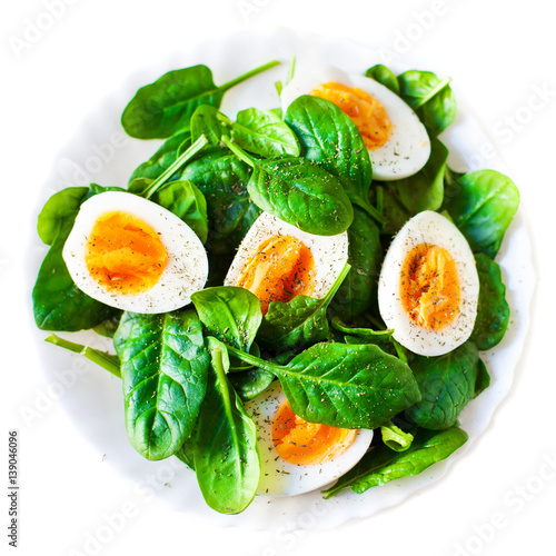 Boiled halved eggs on plate decorated with spinach leaves isolated on white. Healthy salad