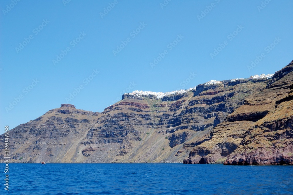 Fototapeta premium Waterless shore of the island of Santorini, Greece. Few people have adapted to live on this volcano. Sailing around the island by tour boat. From a trip to the Cycladic Archipelago