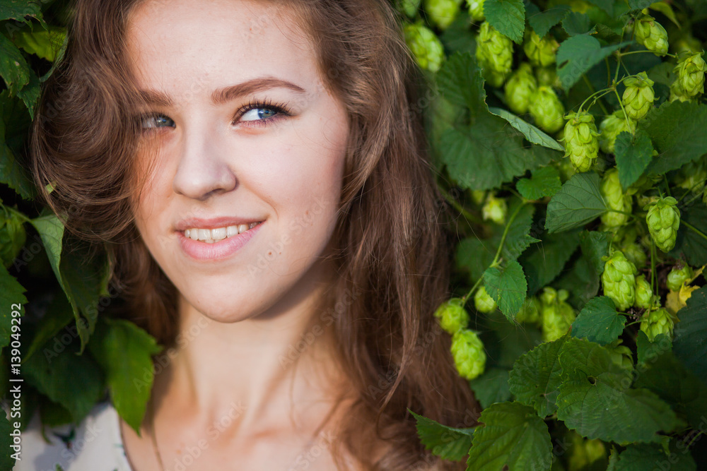 Young beautiful girl smiling in fresh green branches of hop, closeup portrait Young beautiful girl smiling in fresh green branches of hop, closeup portrait