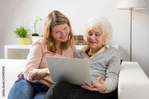 Granddaughter teaching grandma how to use laptop computer