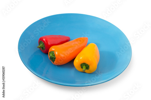 Three small colorful peppers on a blue plate