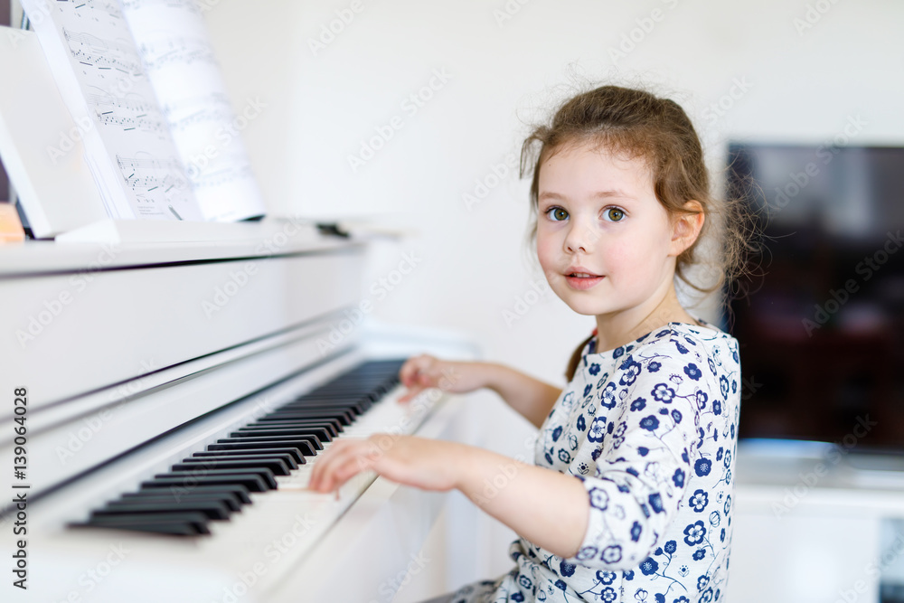 Fototapeta Beautiful little kid girl playing piano in living room or music school