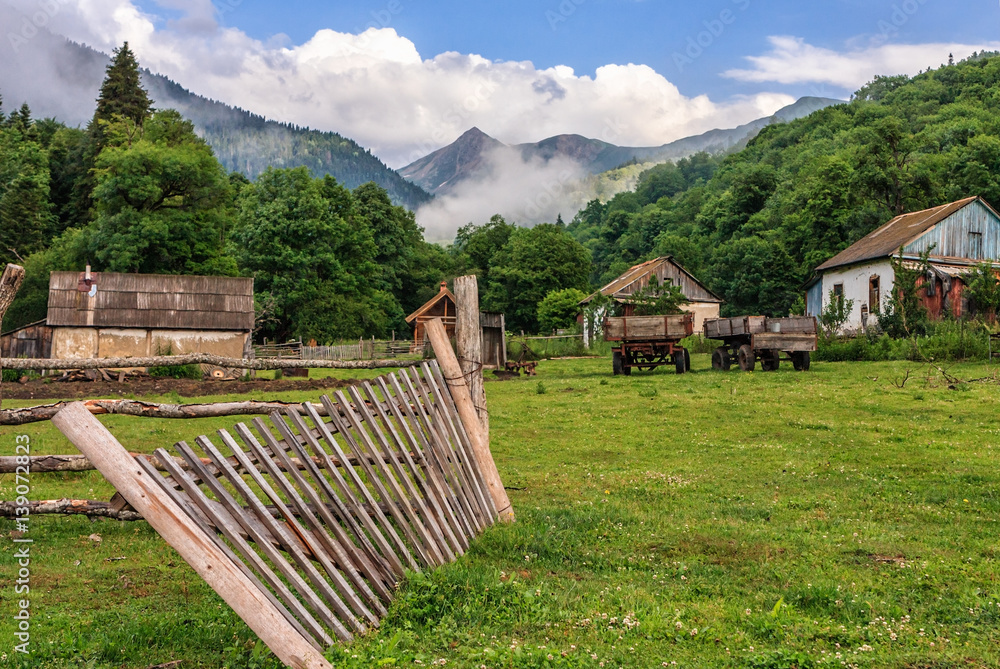 Scenic rustic landscape of peaceful Russian countryside life in Caucasus mountains with mountain peak and blue sky at summer