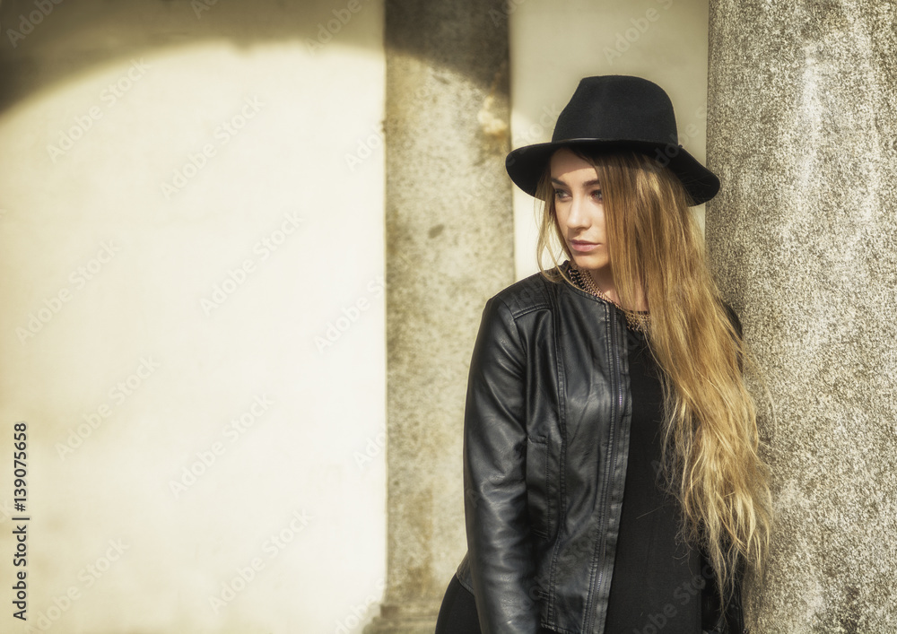 Portrait of attractive blonde young woman in black fedora hat and leather jacket looking at camera Portrait of attractive blonde young woman in black fedora hat and leather jacket looking at camera