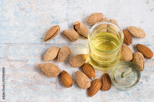 Almond oil. Almond oil in a glass bottle and almond nuts on a light wooden background.