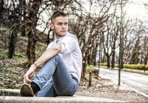 Portrait of handsome young man looking to a side while sitting in city park