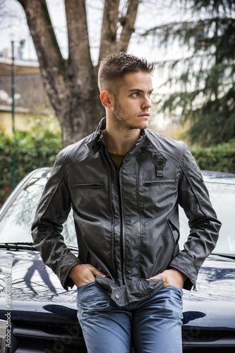 Portrait of young handsome man leaning on his new car, outdoor in city setting