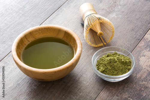 Matcha green tea in a bowl and bamboo whisk, on wooden background

