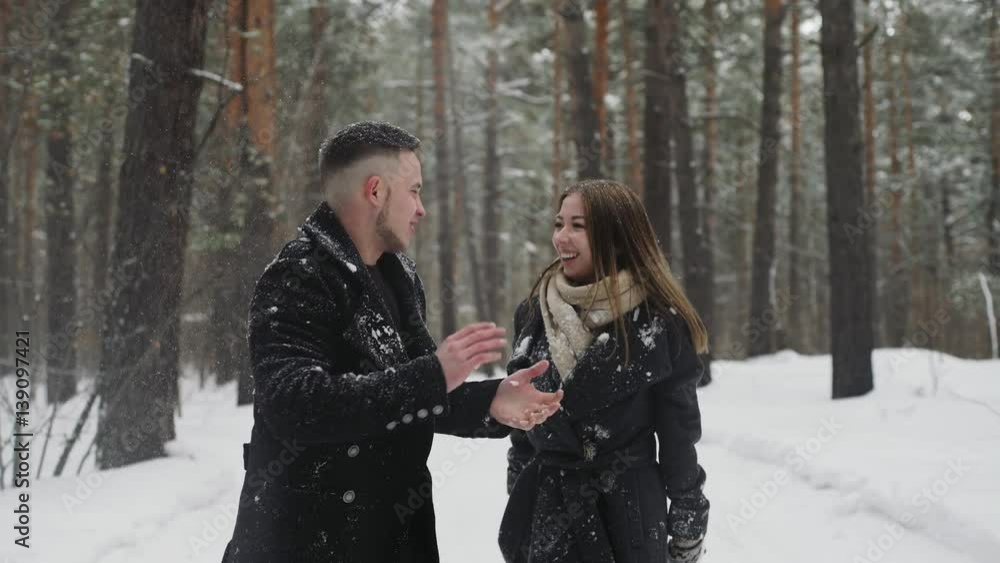 20s young couple is throw snow behind and have a fun in winter forest 20s young couple is throw snow behind and have a fun in winter forest