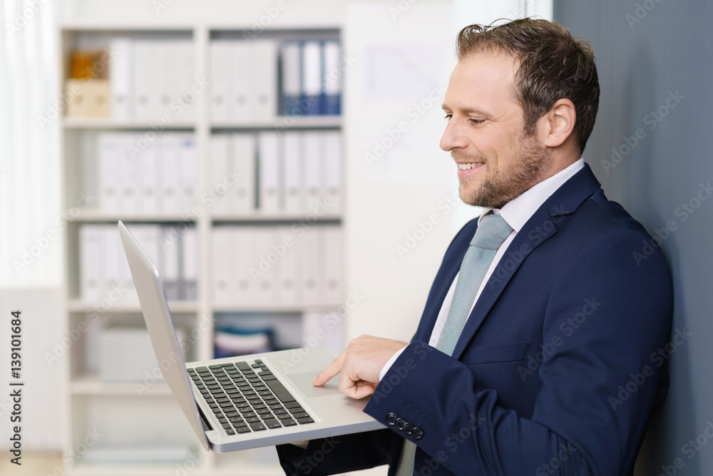 geschäftsmann steht im büro und schaut auf sein notebook geschäftsmann steht im büro und schaut auf sein notebook