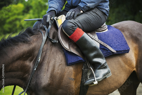 Close up of a rider wearing black riding boots, sitting on a bay horse.