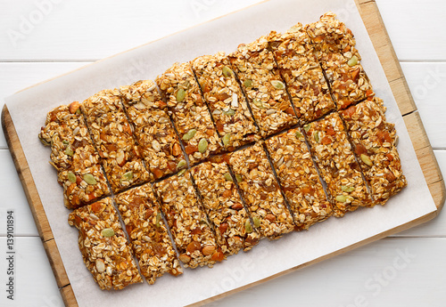 Homemade no bake granola bars with oat flakes, honey, dried apricots and seeds on white baking paper.