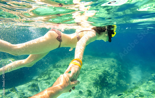 Snorkel couple swimming together in tropical sea with follow me composition - Snorkeling tour in exotic diving scenarios - Fun travel concept with active girl underwater - Soft focus due water density