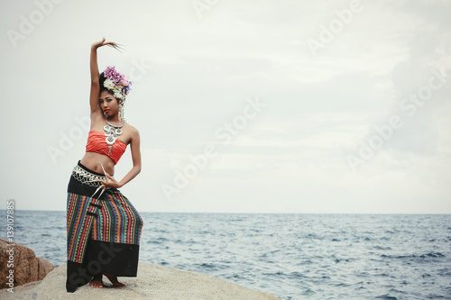 Portrait of dancing Thai girl in Thailand traditional dress with flowers on her hair style on sea shore