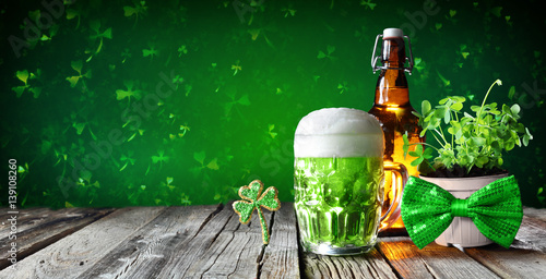 Fotografia St Patrick's Day - Green Beer In Glass With Bottle And Clovers On Wooden Table
