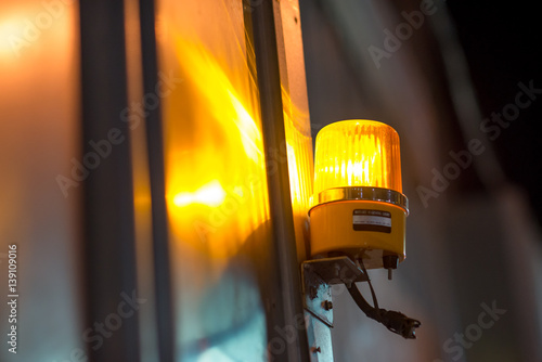 Close-up detail of a yellow revolving warning light shining onto a metal wall at a construction site. Industry and construction concept.