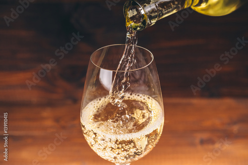 Pouring white wine from a bottle in a wineglasses on wooden background. Free space