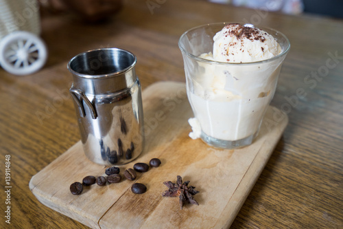 a shot of coffee in metal pitcher and vanilla ice-cream are stand on rustic wooden chopping board © Mongkol