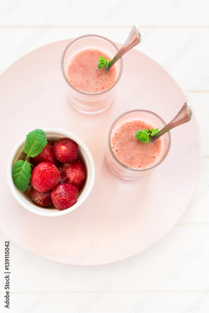 Two glasses with fresh strawberry and banana smoothie decorated mint leaves on white wooden background. Selective focus Two glasses with fresh strawberry and banana smoothie decorated mint leaves on white wooden background. Selective focus