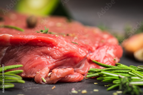 Fresh raw beef meat with avocado and herbs on the black stone background
